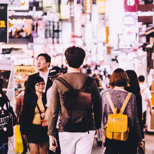 A man with a backpack walking through a crowded Seoul street.